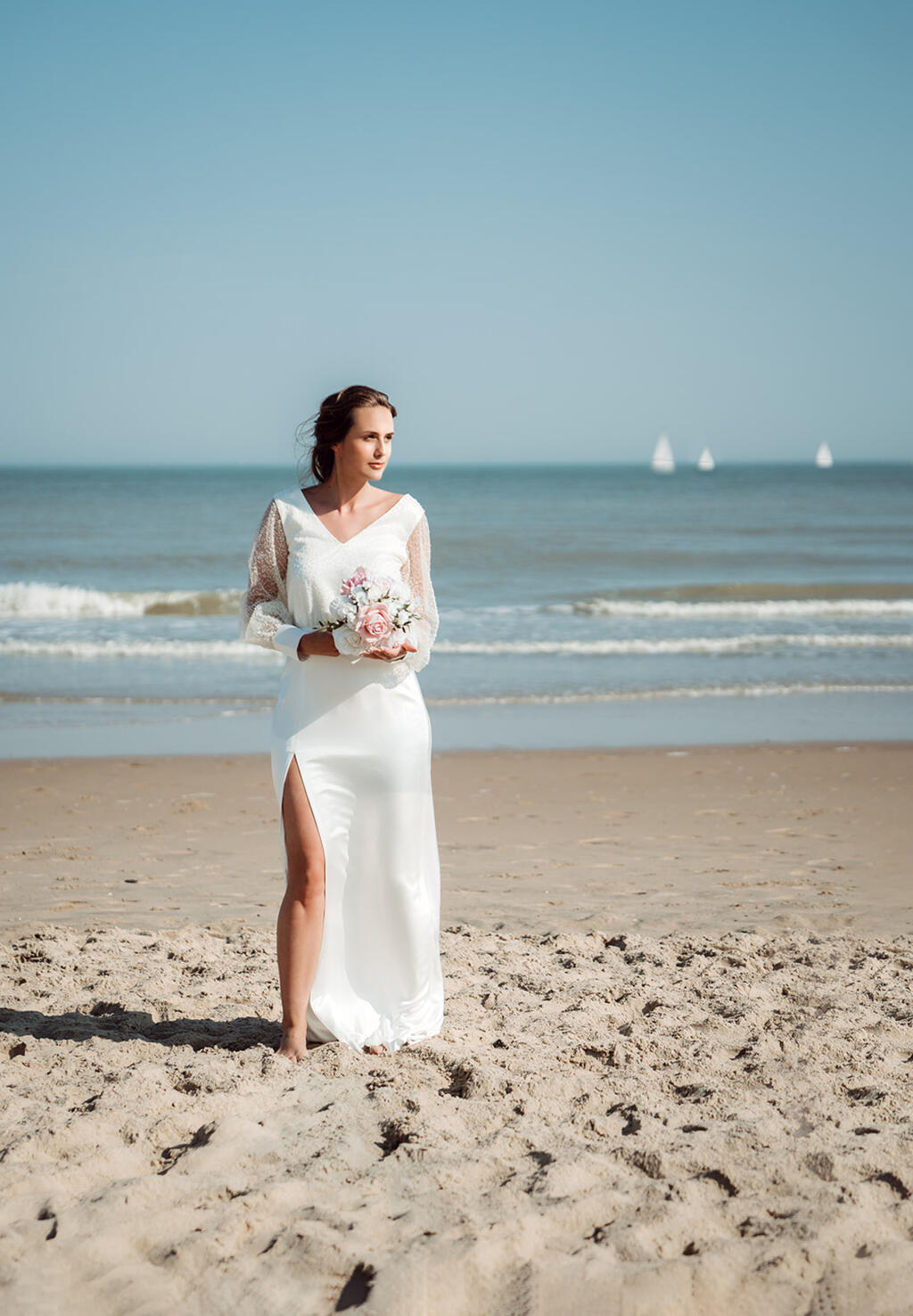 bruid-op-strand-elegante-trouwjurk-met-hoge-split-vooraan-en-top-in-parelstof-met-pofmouwen.jpg